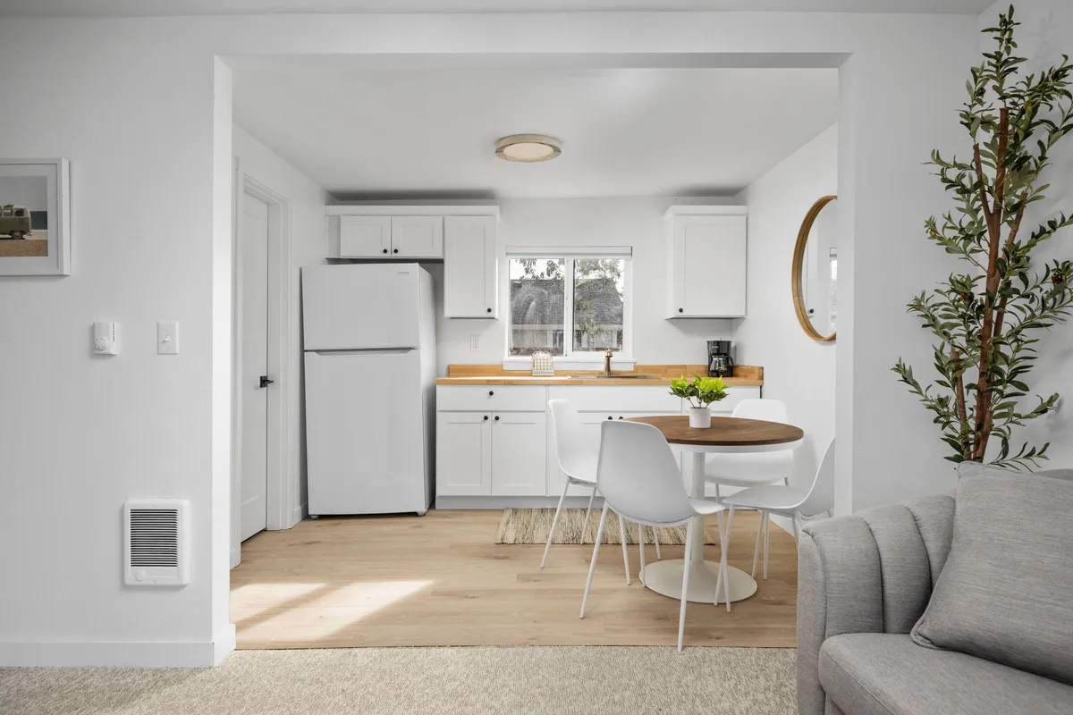 A welcoming kitchenette and dining area with a dining table, white refrigerator, and kitchen cabinets. The window lets in abundant sunlight, creating a cheerful setting for casual meals, morning coffee, or entertaining guests.