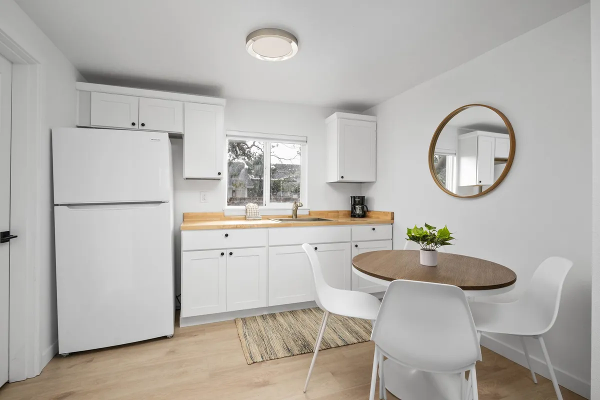A bright and cheerful dining space with a wooden countertop, round dining table, potted plant, and a large mirror. The open layout provides enough room for pets to move around comfortably while their owners dine or socialize.