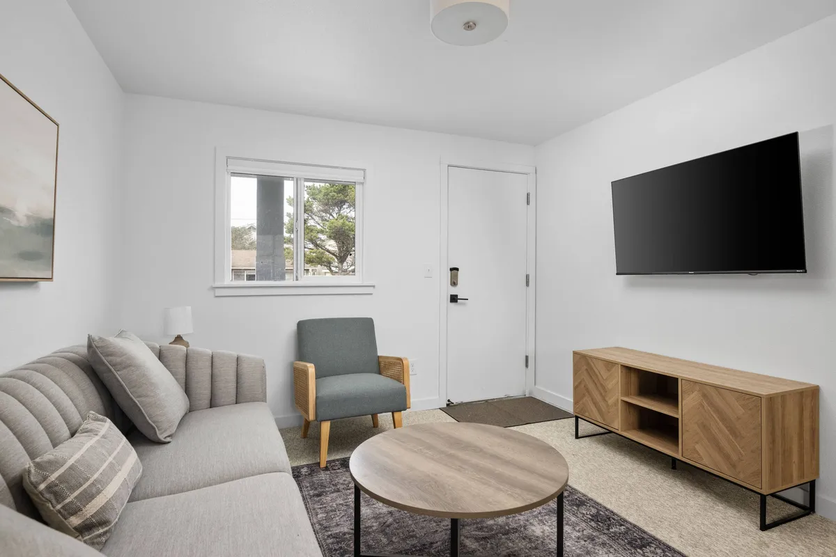 A cozy living area featuring a plush sofa, coffee table, armchair, and TV set near a large window. The space is filled with natural light, creating a relaxing atmosphere ideal for socializing, watching movies, or enjoying quiet moments together.