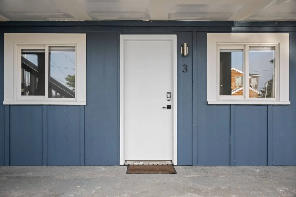 The inviting exterior of the inn, showcasing the front door, windows, and the number 3. The image captures guests arriving, socializing with neighbors, and enjoying quiet moments by the windows or on the porch.
