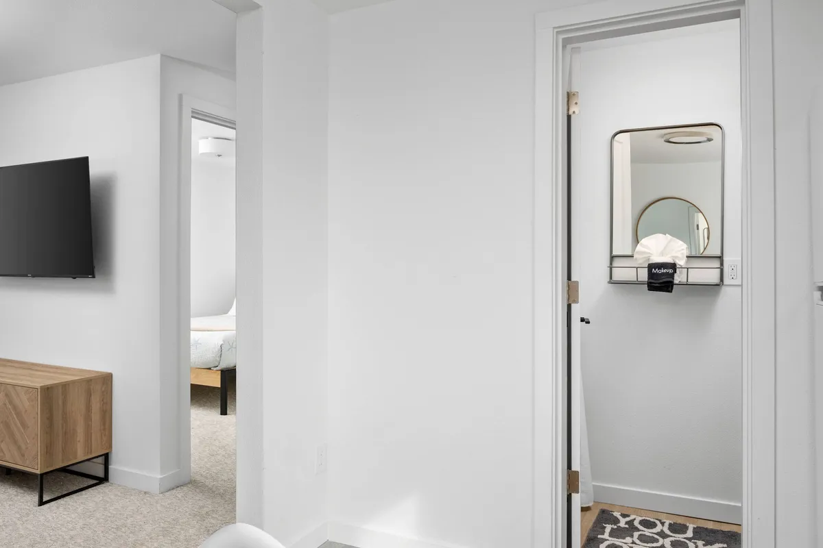A comfortable living area featuring a wall-mounted TV, a wooden console table, and a round-framed mirror. The modern furnishings and open space create a cozy environment ideal for relaxing with your pets after a day at the beach.