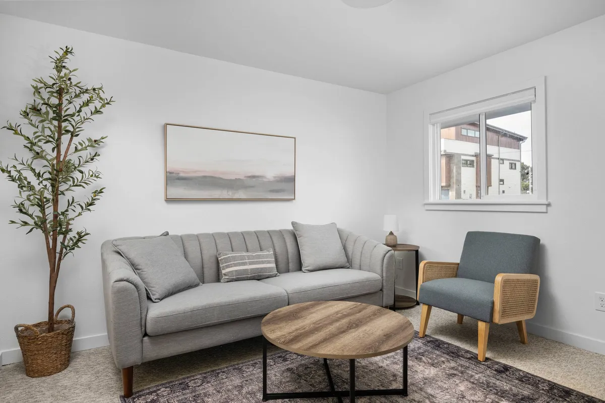 A stylish and comfortable living space with a cozy sofa, elegant coffee table, tasteful artwork, potted plant, and a light-filled window. The décor is modern yet welcoming, perfect for reading, relaxing, or hosting small gatherings.